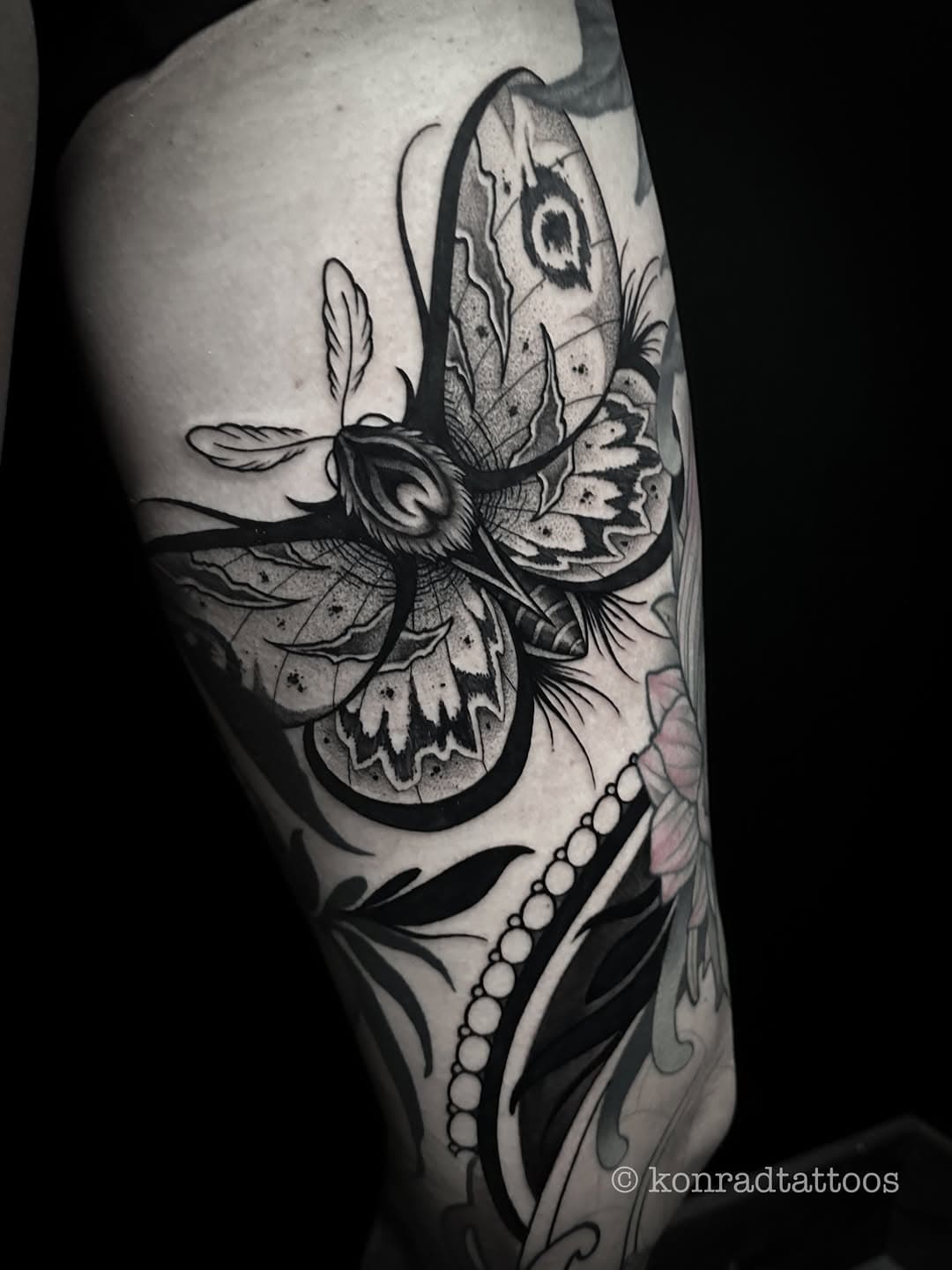 Black and grey moth tattoo with detailed wings, crystals, feathers and decorative elements on arm in illustrative blackwork style
