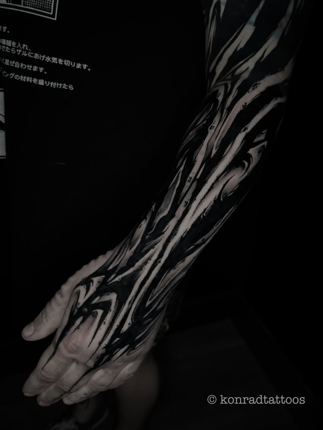 Dynamic blackwork arm tattoo featuring bold flowing brushstroke designs in black and grey ink by Konrad Tattoos