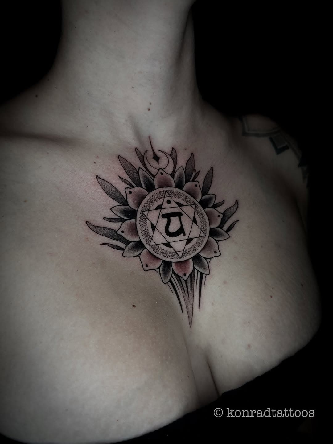 Blackwork chest tattoo featuring a lotus flower mandala with geometric patterns and a Sanskrit symbol in the center