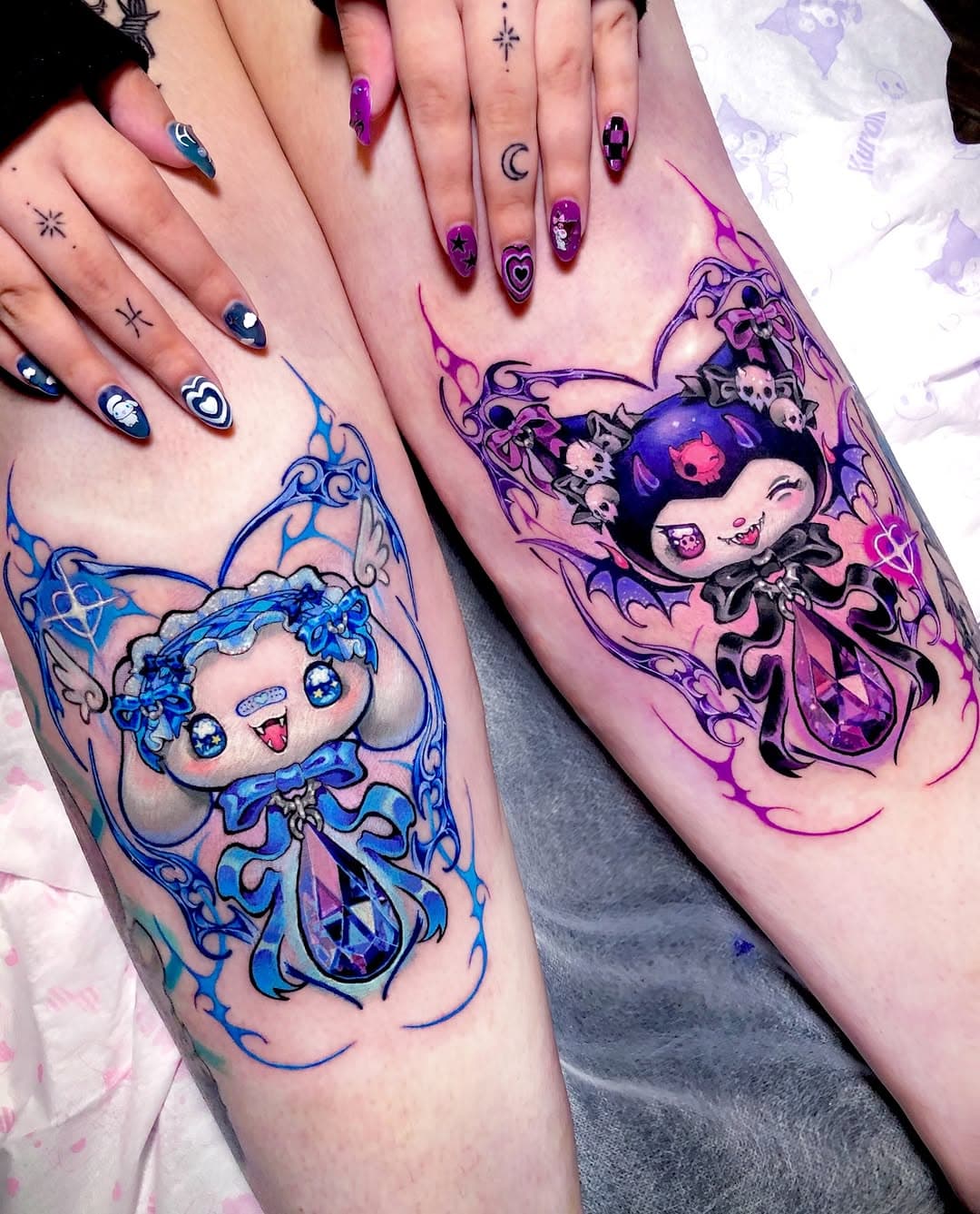 Matching anime-style mermaid tattoos in blue and purple with ornate frames, skulls, and gems on two people's forearms with coordinating nail art