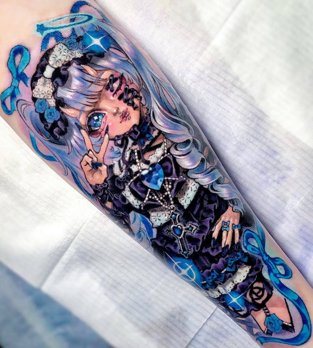 Colorful anime-style tattoo of a girl with long flowing hair in blue, purple, and pink tones with decorative elements and ribbons