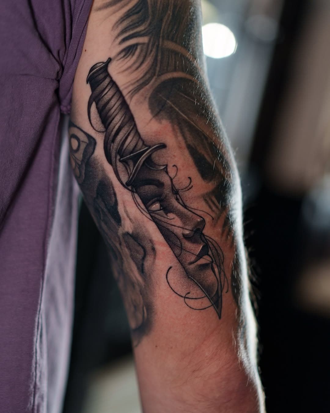 Black and grey illustrative forearm tattoo featuring a feminine face with flowing hair and decorative linework in dotwork style