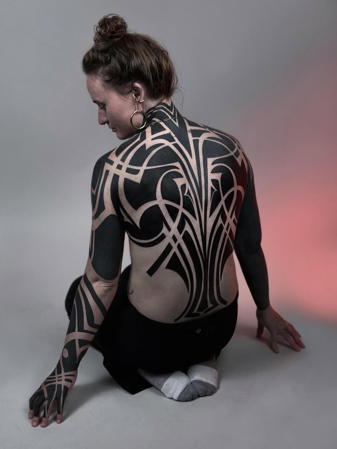 Large-scale blackwork tribal tattoo covering back and arms with bold geometric curves, spirals and interlocking ornamental patterns