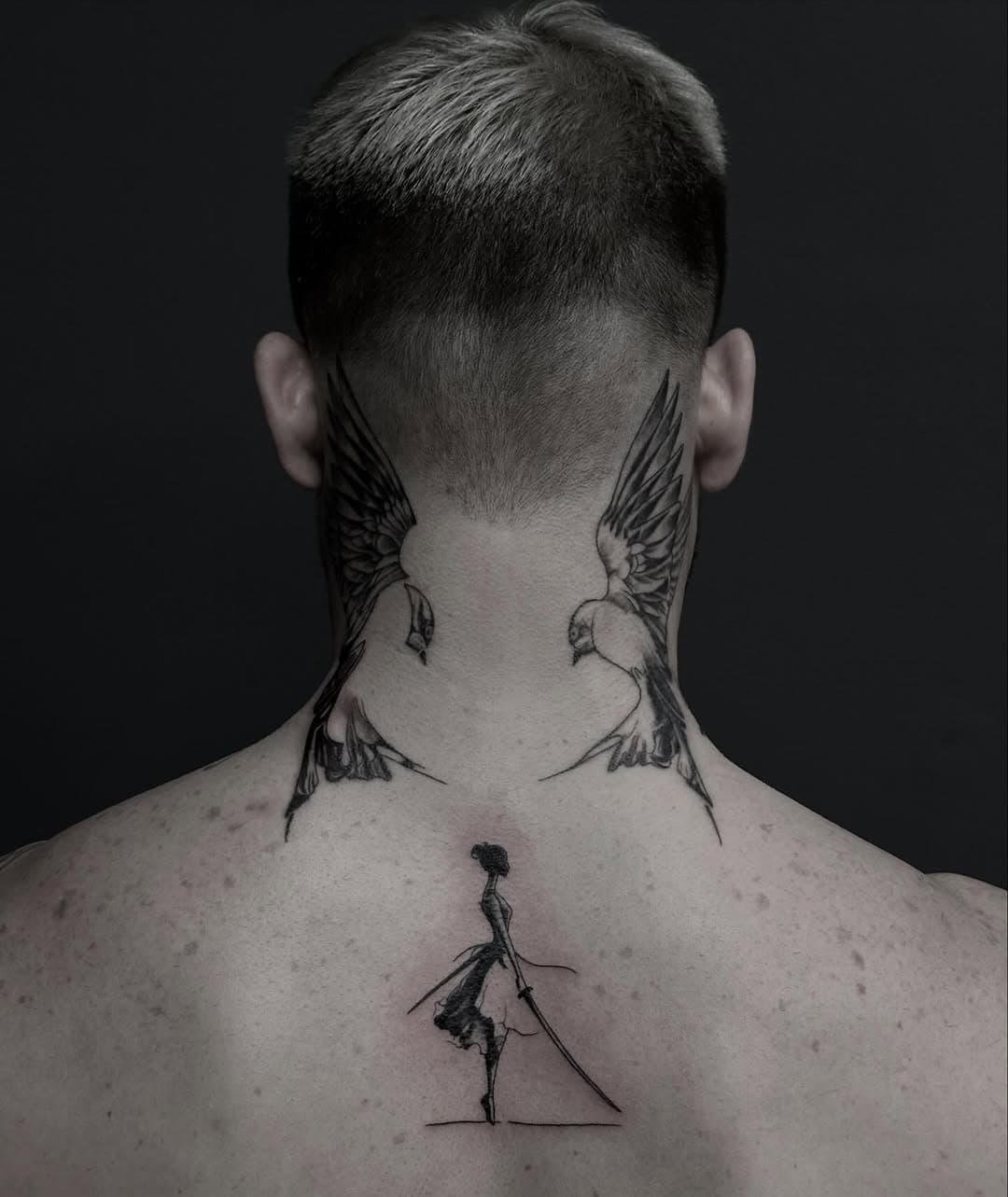 Back and neck tattoo featuring two symmetrical swallows in flight flanking a single wilted rose stem in sketch style black ink