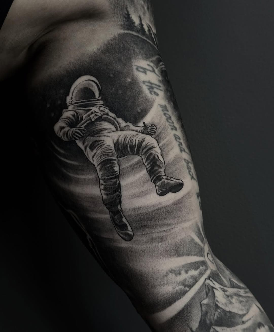 Black and grey realism tattoo of an astronaut floating in space on forearm, surrounded by cosmic elements and shading