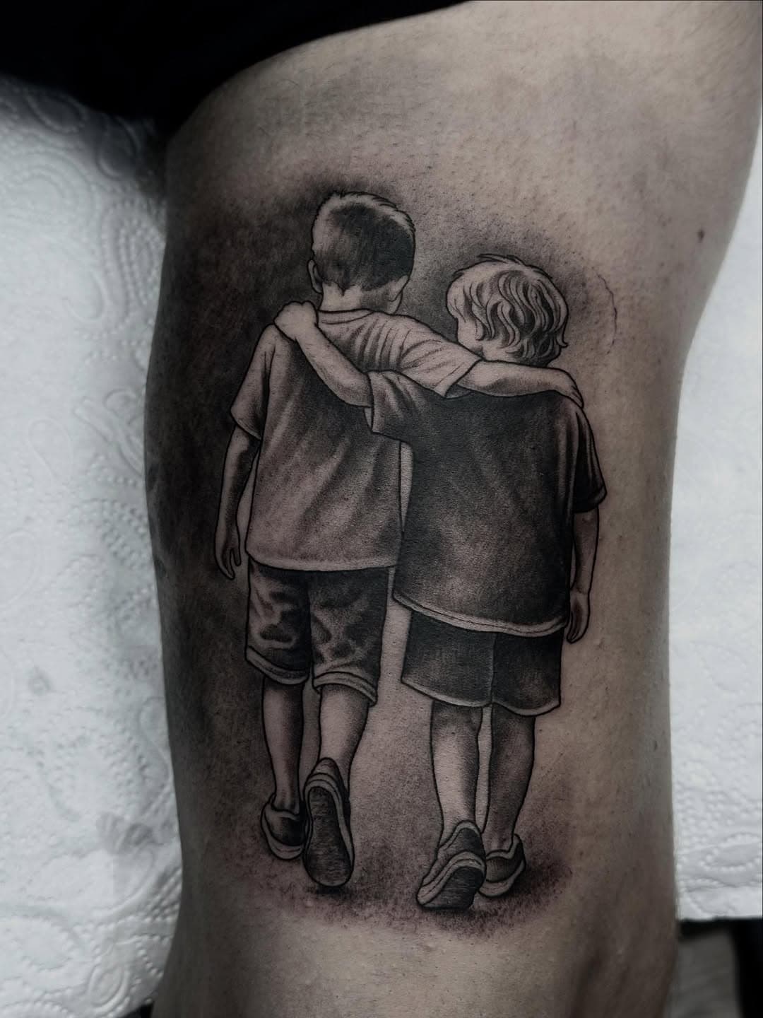 Black and grey realistic tattoo of two young boys with arms around each other's shoulders, viewed from behind