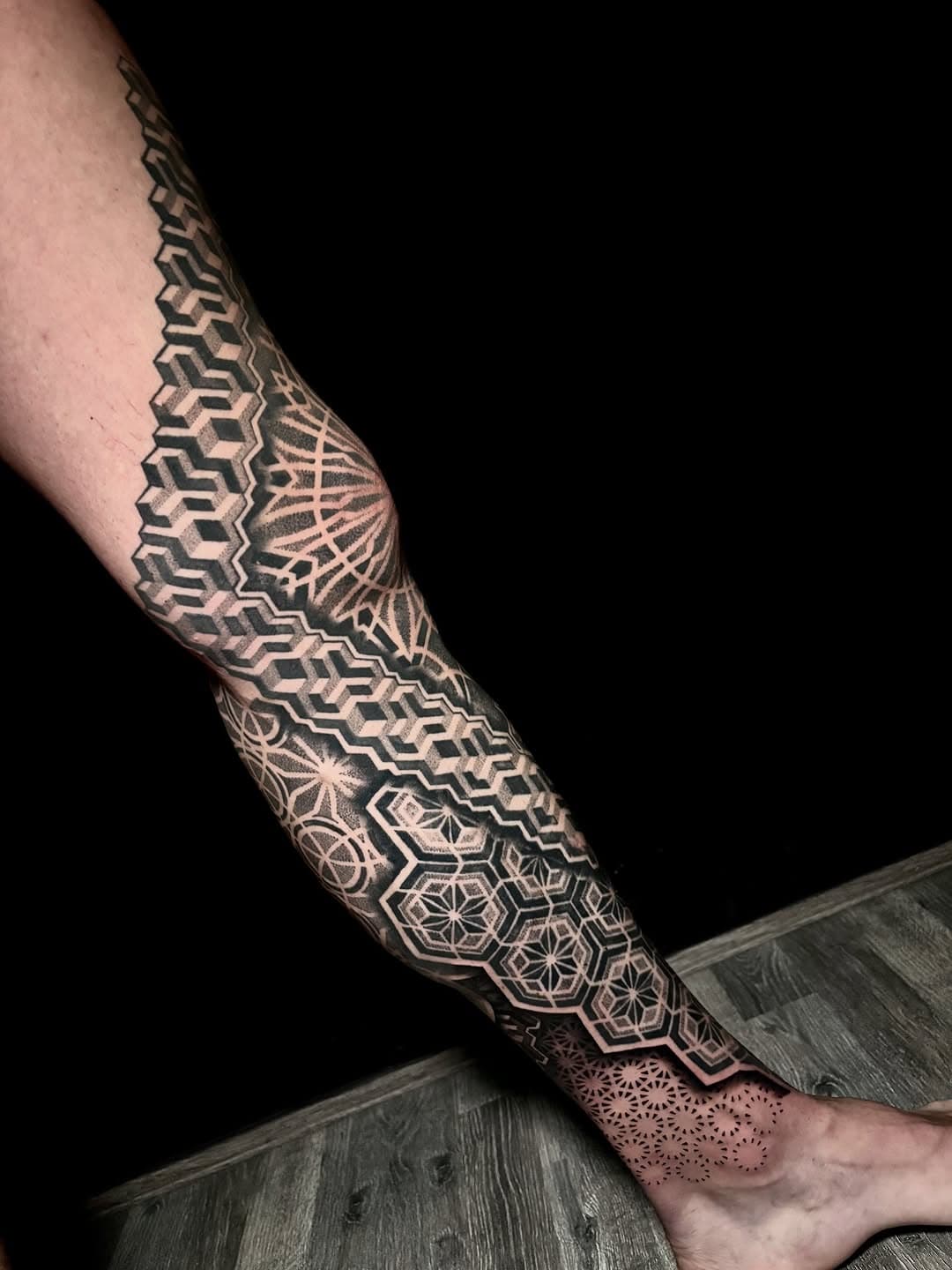 Intricate geometric blackwork leg sleeve tattoo featuring hexagonal patterns, sacred geometry, and mandala designs flowing from calf to ankle