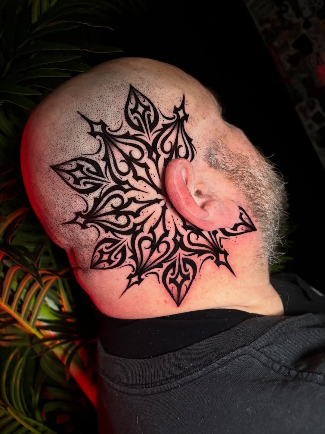 Intricate geometric blackwork mandala tattoo on side of shaved head wrapping around ear with ornate tribal patterns