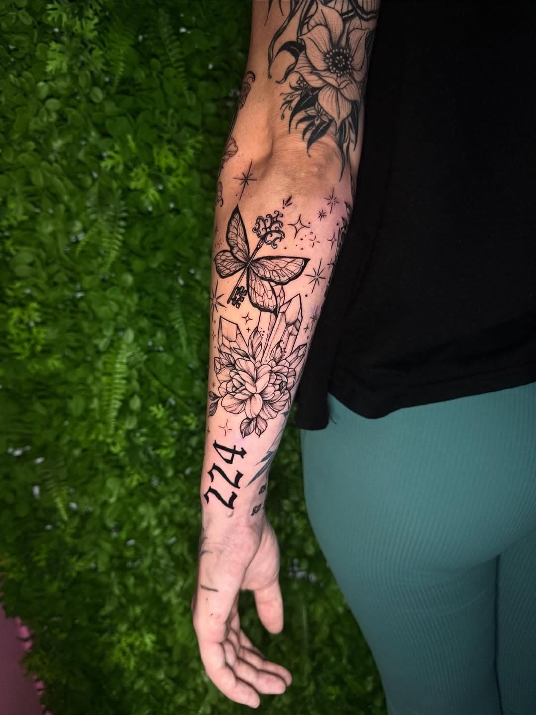 Black-and-grey floral sleeve tattoo featuring butterfly, flowers, stars, and Roman numerals in illustrative blackwork style
