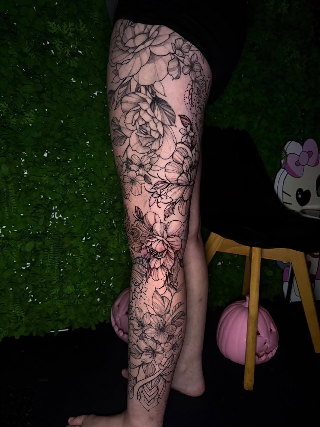Black and grey floral leg sleeve tattoo featuring roses, orchids, and various botanical elements in illustrative blackwork style