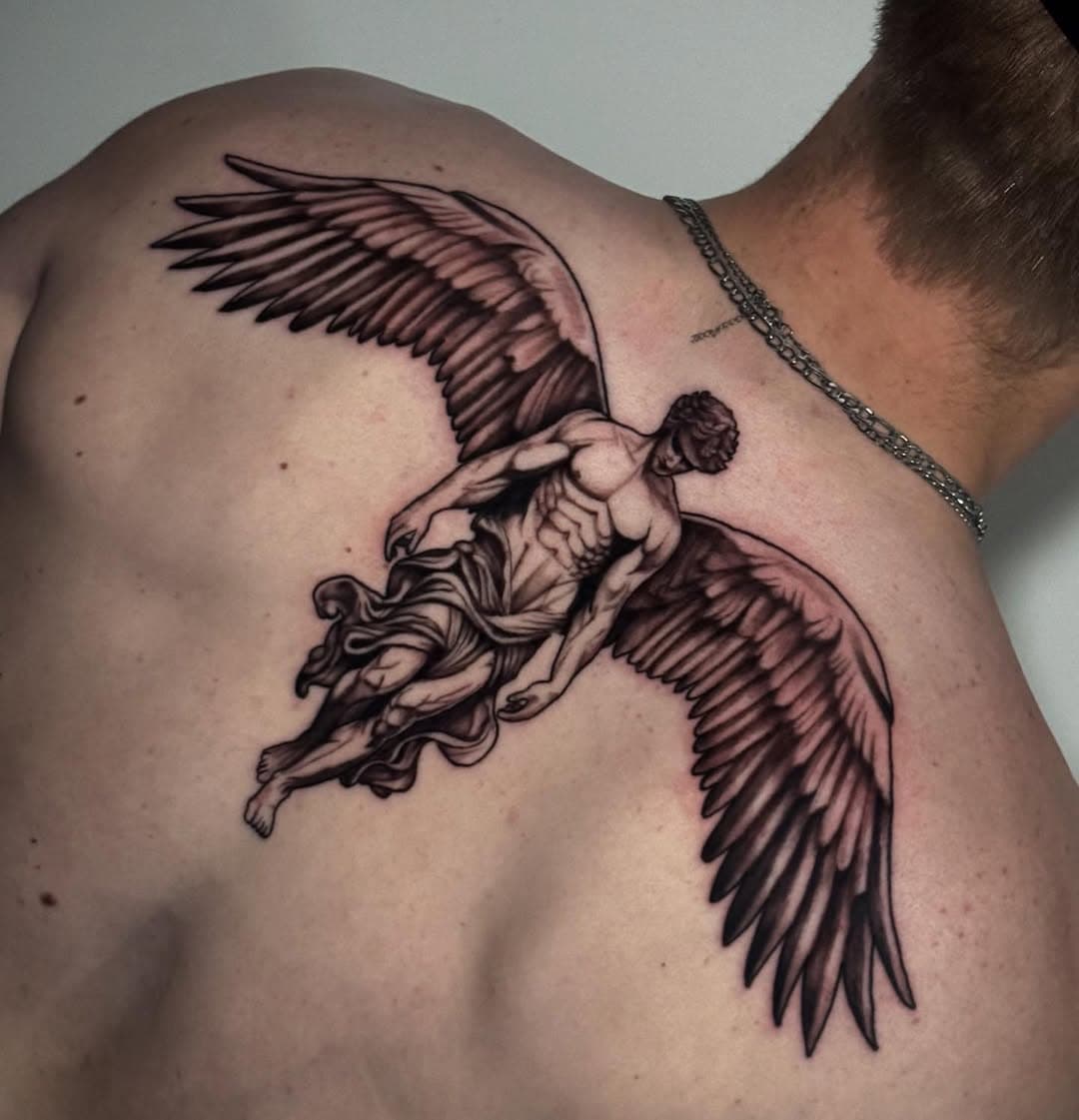 Black and grey tattoo of Icarus with detailed wings spread across upper back, depicting the Greek mythological figure in flight