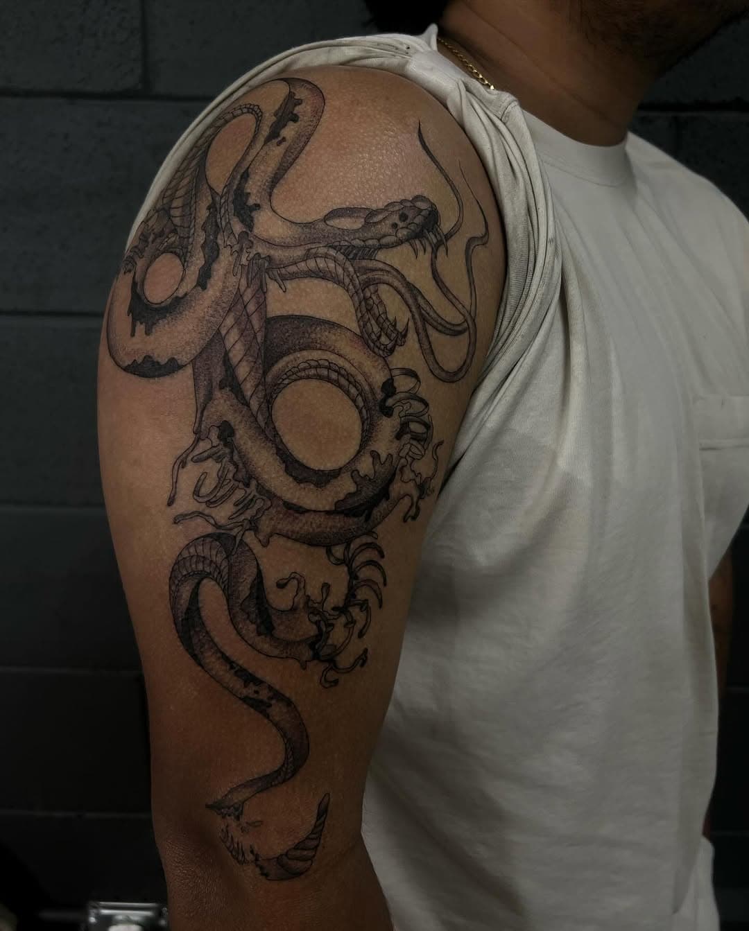 Black and grey illustrative tattoo of intertwined serpents and dragon wrapped around upper arm and shoulder in detailed linework