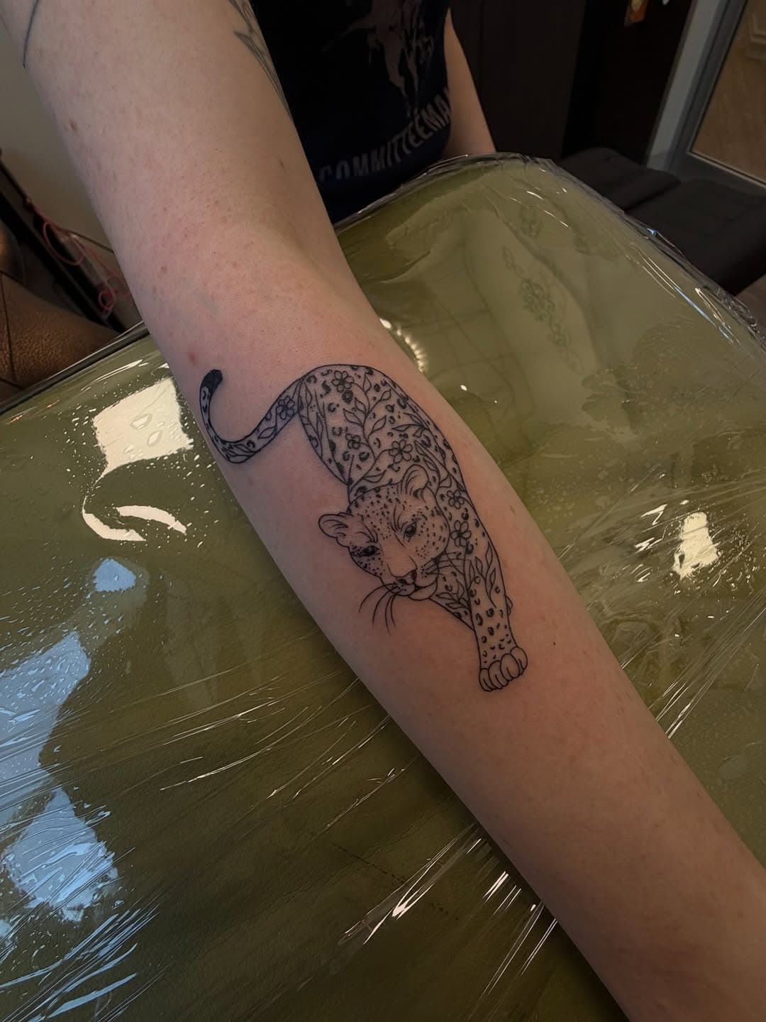 Black and grey illustrative leopard tattoo on forearm showing detailed spotted pattern and flowing tail design