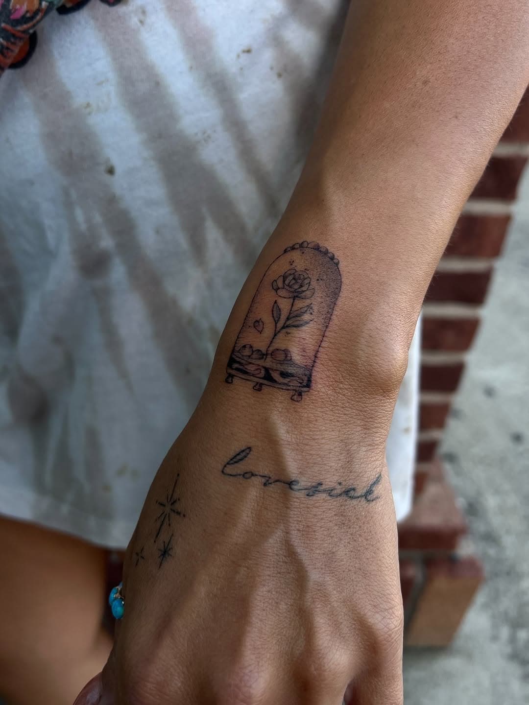 Black and grey tattoo on forearm featuring Beauty and the Beast rose under glass dome with cursive script text below