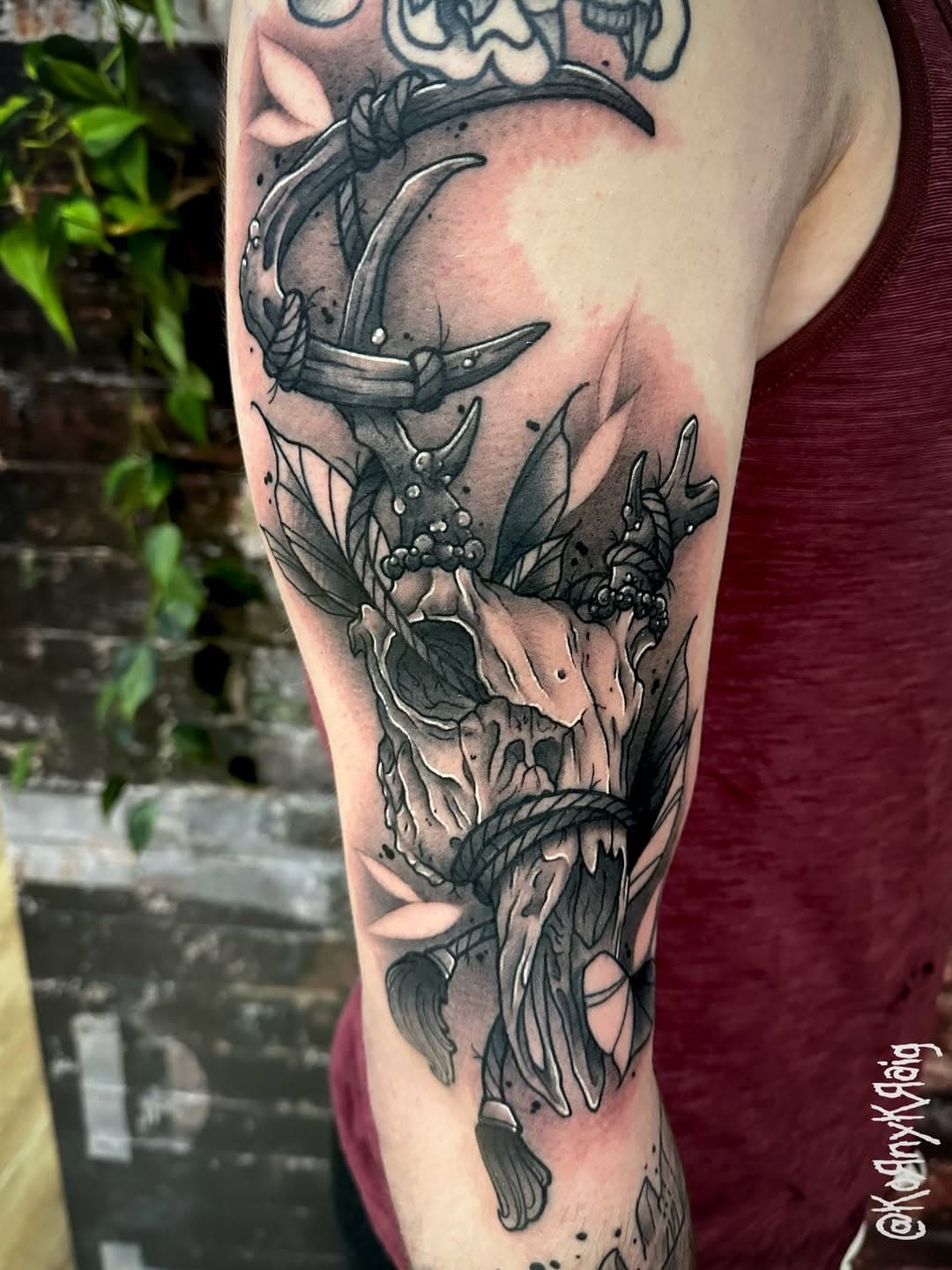 Neo-traditional black and grey arm tattoo featuring a crescent moon, skull, and flowing botanical elements in a surreal composition
