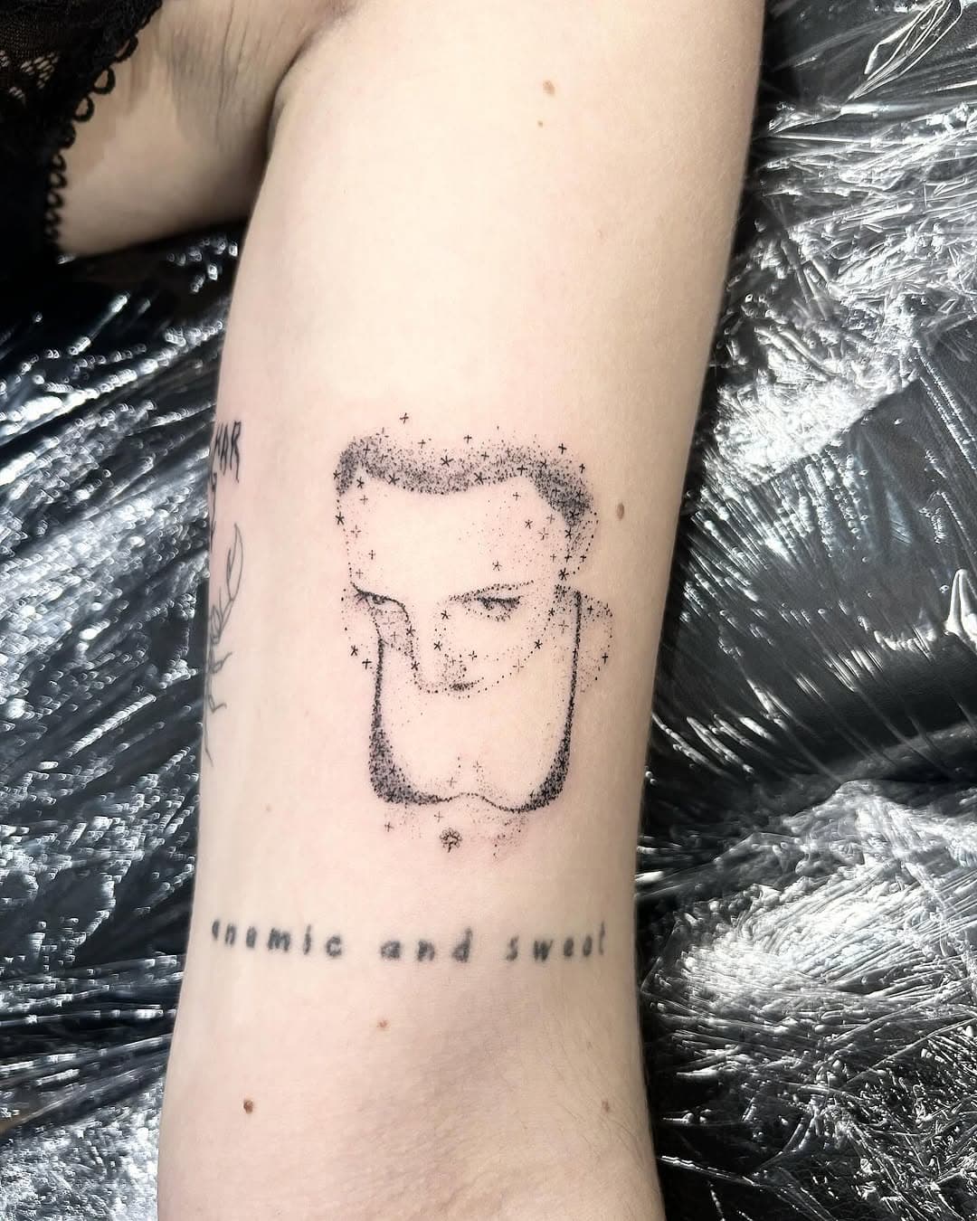 Dotwork tattoo of a contemplative figure with flowing hair on forearm, with text reading cosmic and sweet below