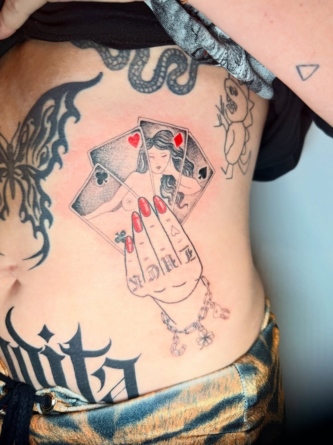 Illustrative tattoo of a hand with red nails holding playing cards featuring a woman, done in fine-line and dotwork style