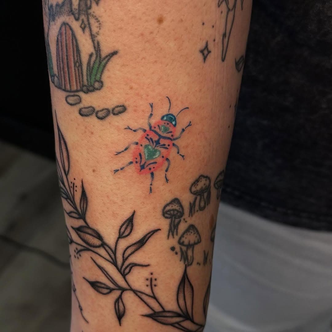 Black-and-grey fine-line tattoo featuring a colorful spider, cactus, botanical leaves, and mushrooms in an illustrative nature-themed design
