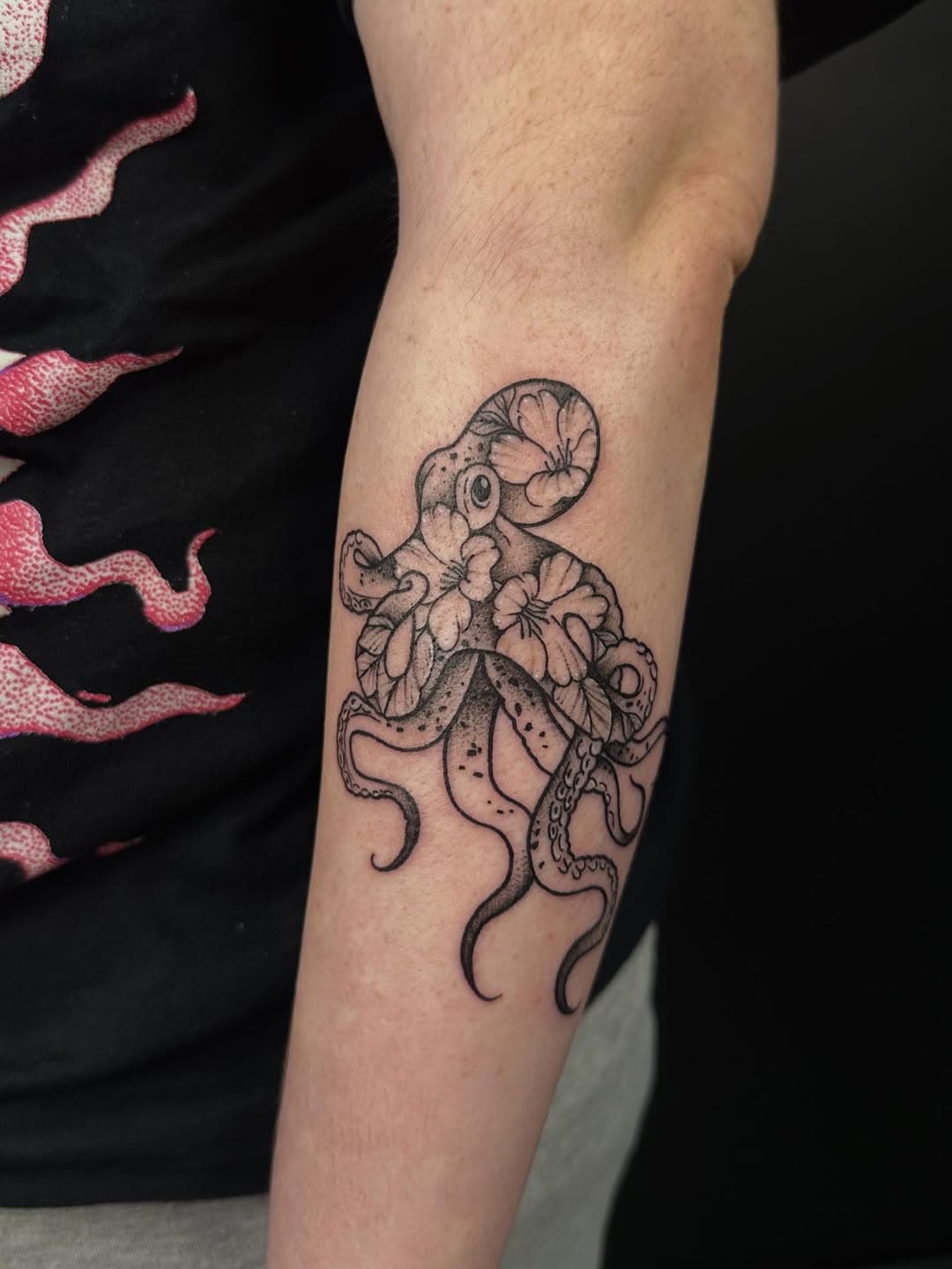 Black and grey fine-line tattoo of an octopus adorned with delicate flowers on forearm in illustrative style