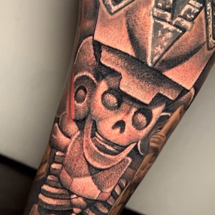 Black and gray neo-traditional tattoo of a smiling cartoon skeleton character wearing a hat on forearm