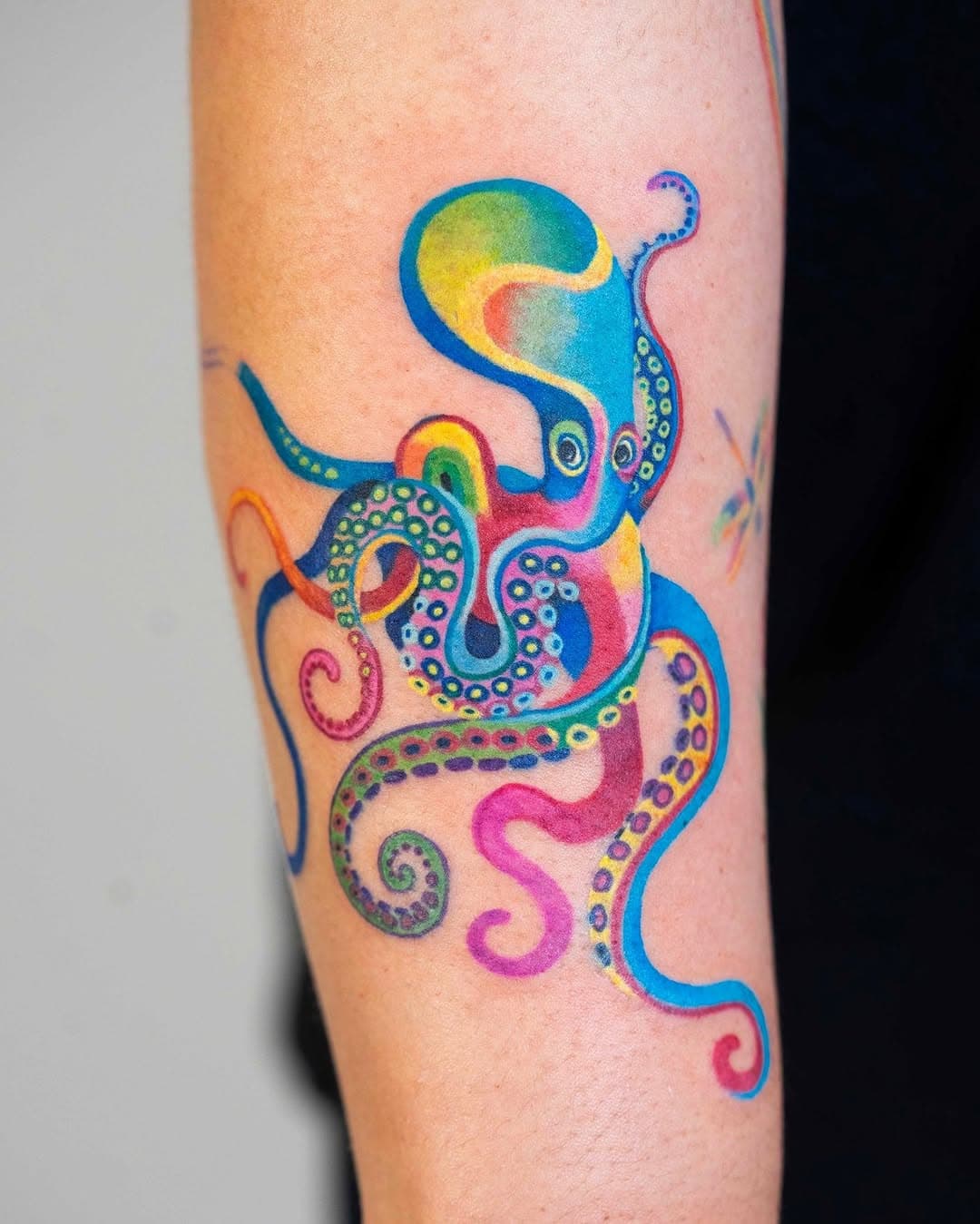 Vibrant watercolor octopus tattoo in rainbow hues with decorative tentacles and sucker details on forearm