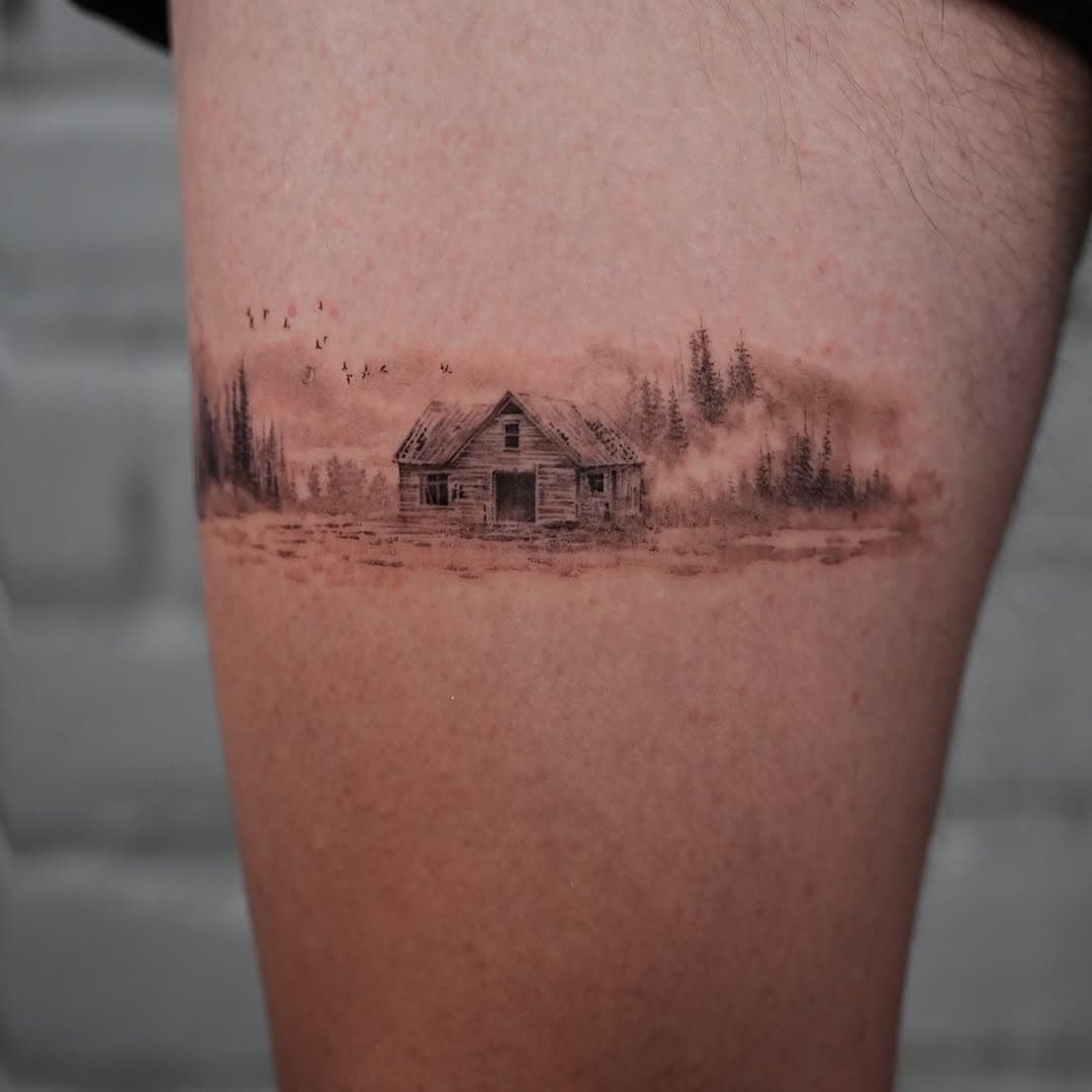 Delicate fine-line tattoo of an abandoned wooden cabin in a misty forest clearing with birds flying overhead and pine trees in the background