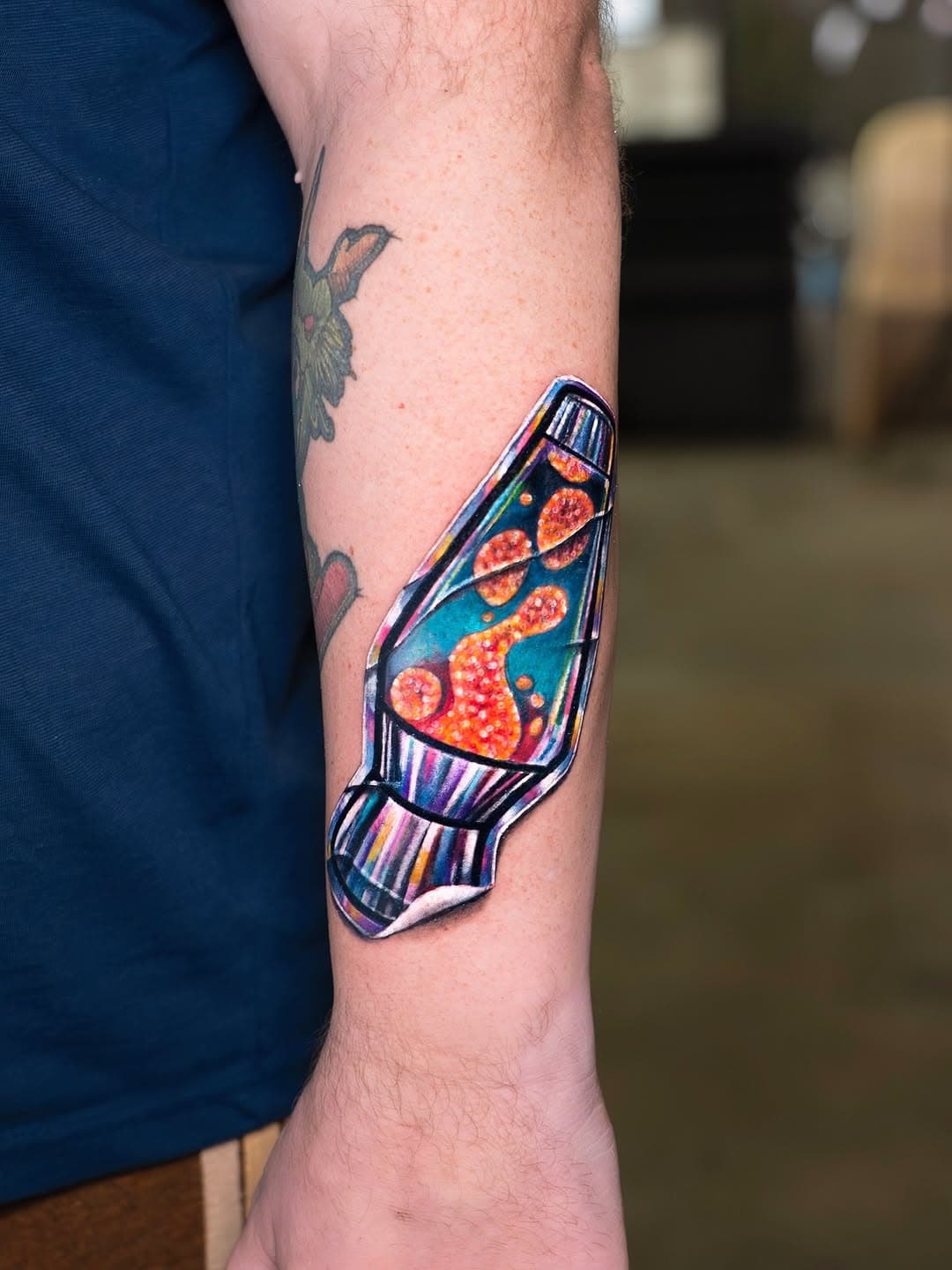 Colorful lava lamp tattoo with vibrant orange and blue wax bubbles in illustrative surrealism style on forearm