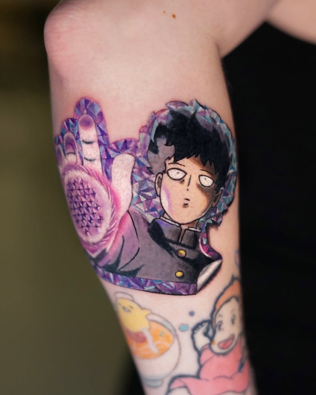 Colorful anime-style tattoo of a character with black hair in dark clothing, surrounded by purple and pink psychic energy effects