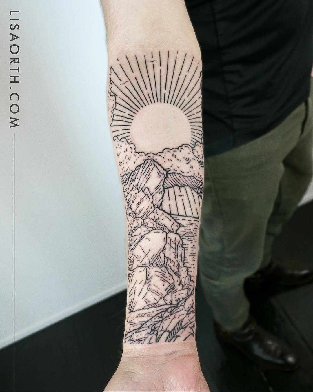 Illustrative fine-line forearm tattoo depicting a mountain landscape with rising sun, clouds, and natural elements in black ink