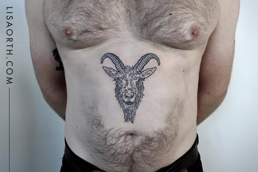 Fine-line illustrative tattoo of a goat head with curved horns on the abdomen, rendered in black ink with detailed linework.