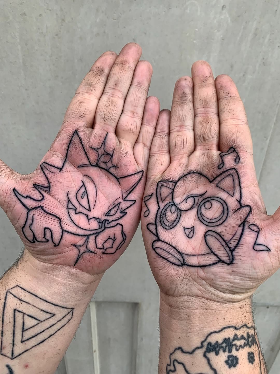 Two palms displaying fine-line tattoos of Pokemon characters - a spiky creature on the left hand and Jigglypuff on the right hand