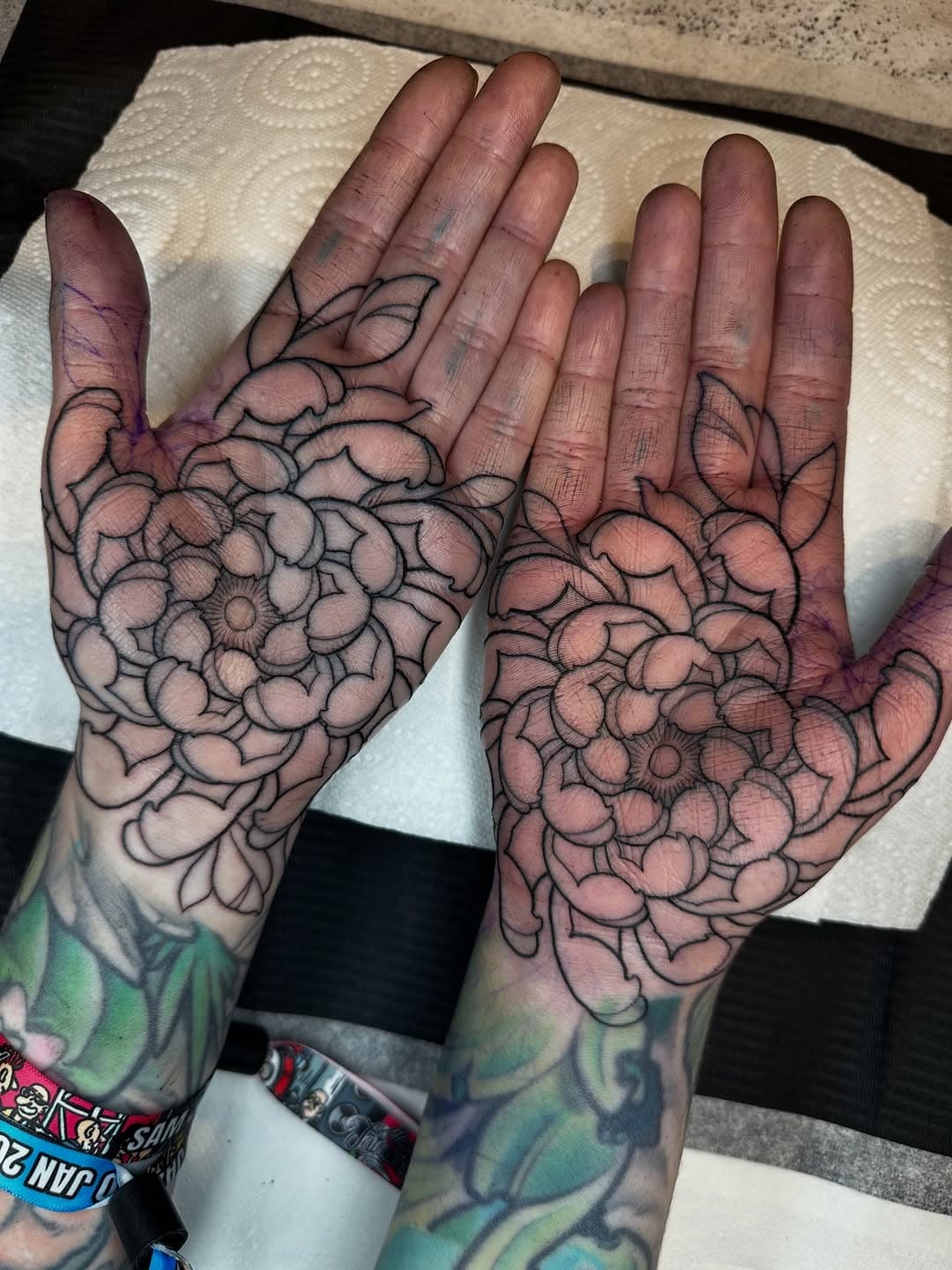 Symmetrical floral mandala tattoos covering both palms in fine black linework, featuring layered petals radiating from center points