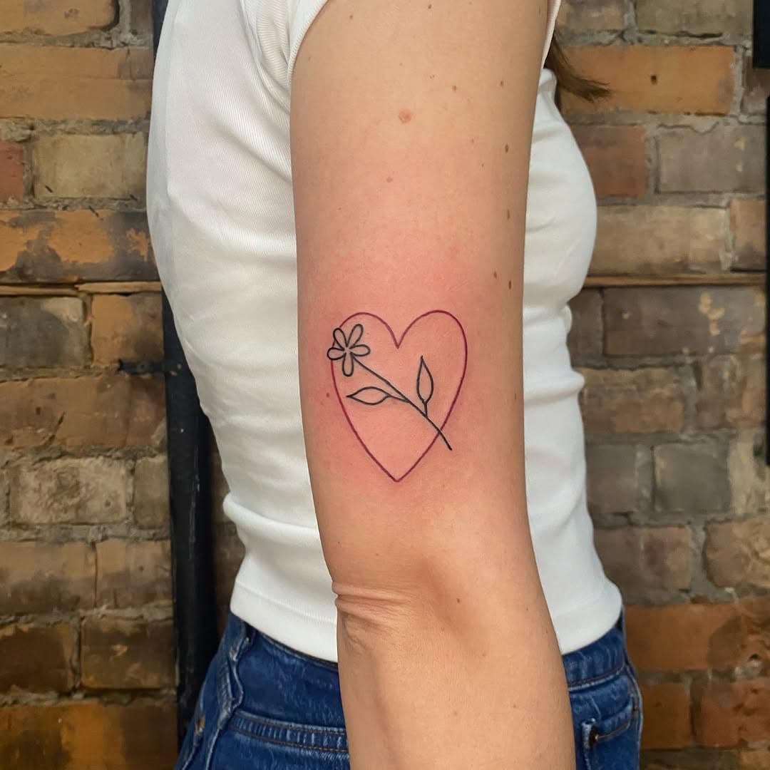 Minimalist fine-line tattoo of a heart outline with a delicate flower stem inside, done in black ink on forearm