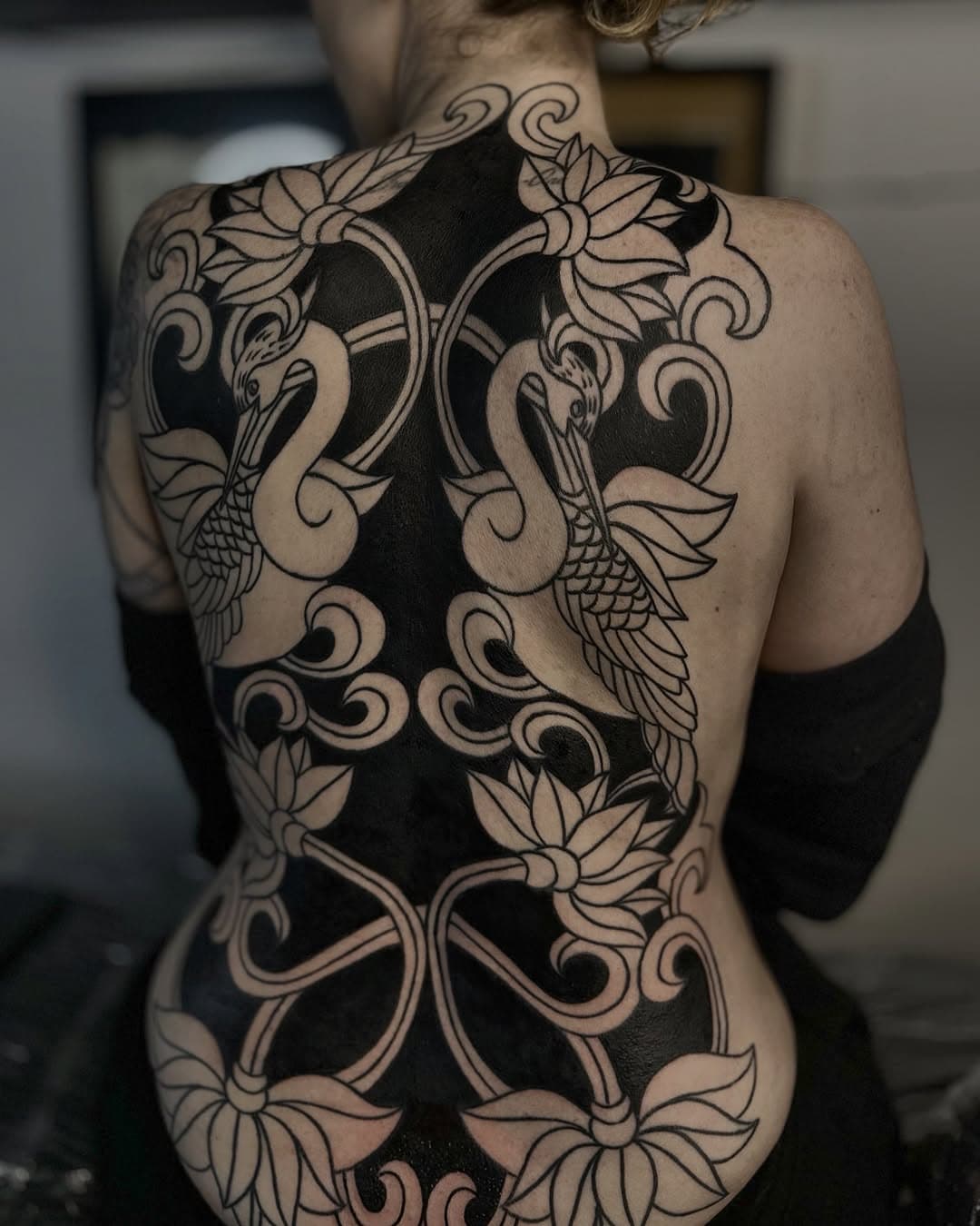 Full back blackwork tattoo featuring symmetrical ornamental design with cranes, lotus flowers, and flowing decorative swirls