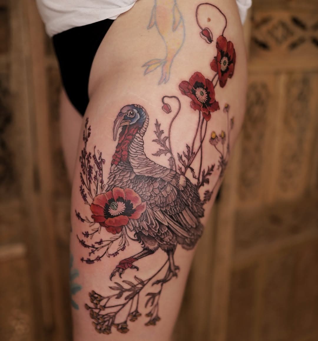 Illustrative tattoo of a turkey with detailed feathers surrounded by red poppies and botanical elements on thigh